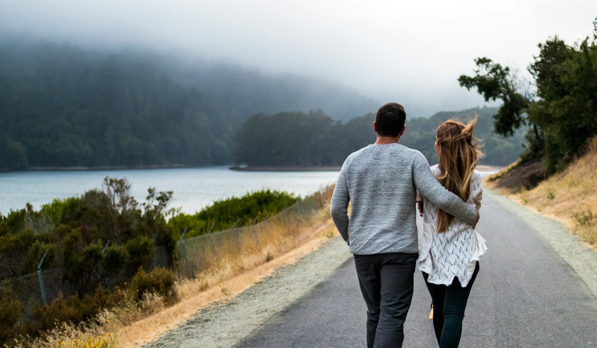 Two travellers walking side by side along an empty road through hills