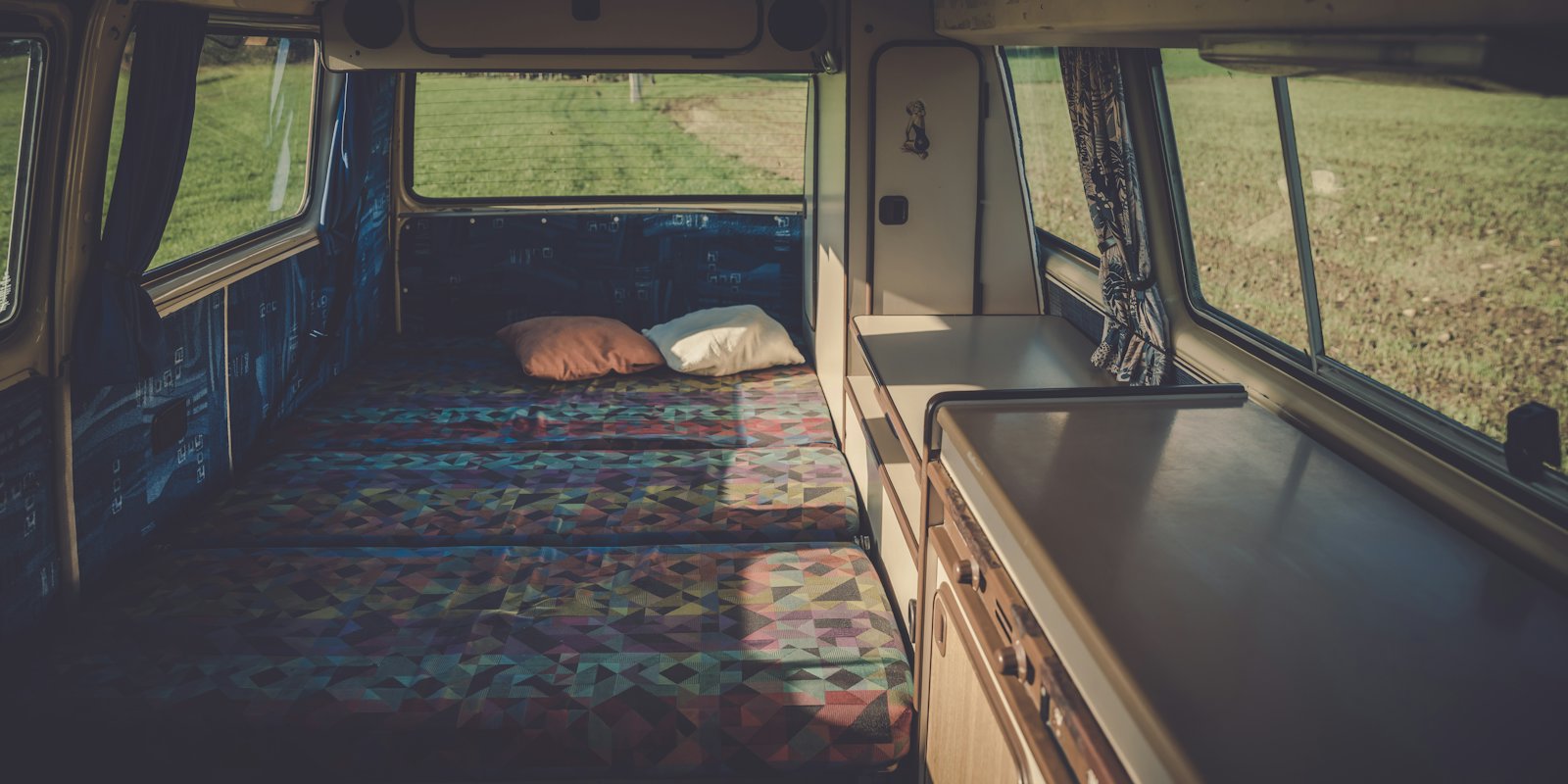 The inside of a campervan with a made-up bed and a window onto the countryside