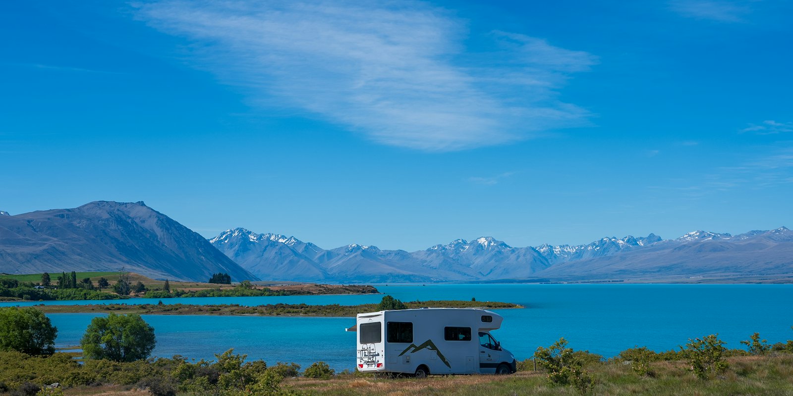 A motorhome parked beside a turquoise lake below mountains in New Zealand