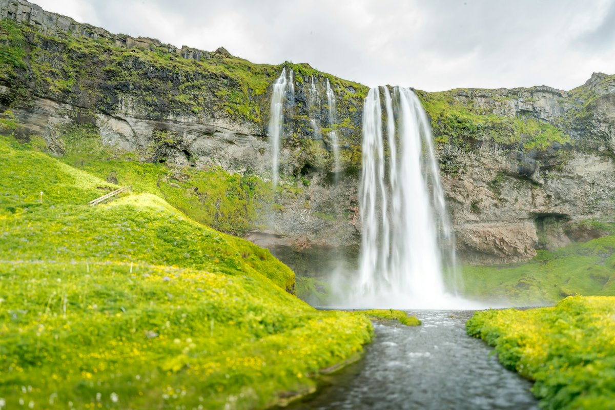 Seljalandsfoss waterfall dropping over a green cliff with a footpath leading to it