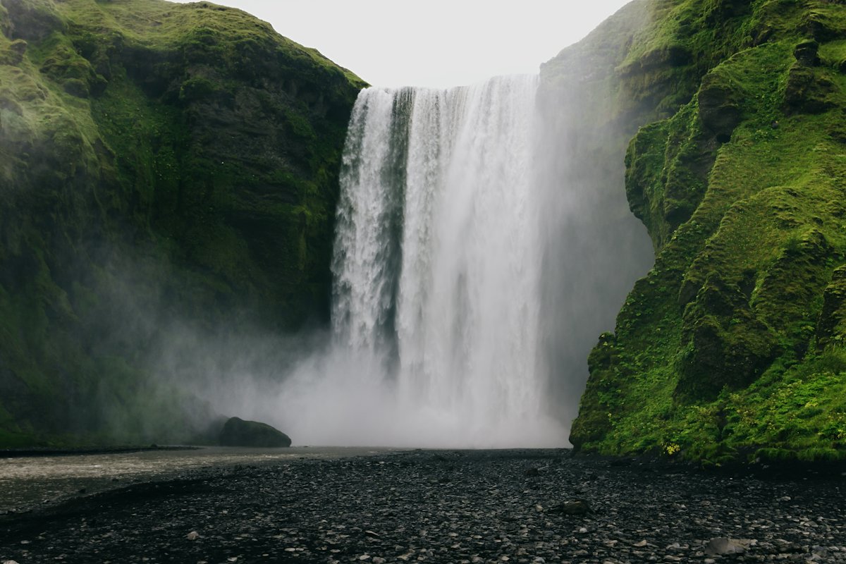 Skógafoss waterfall falling over a mossy green cliff into a river