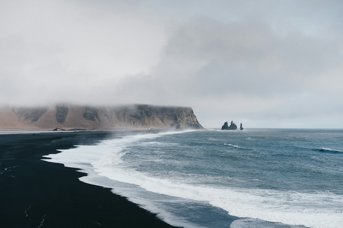 Black sand beach and sea stacks under cloud near Vík