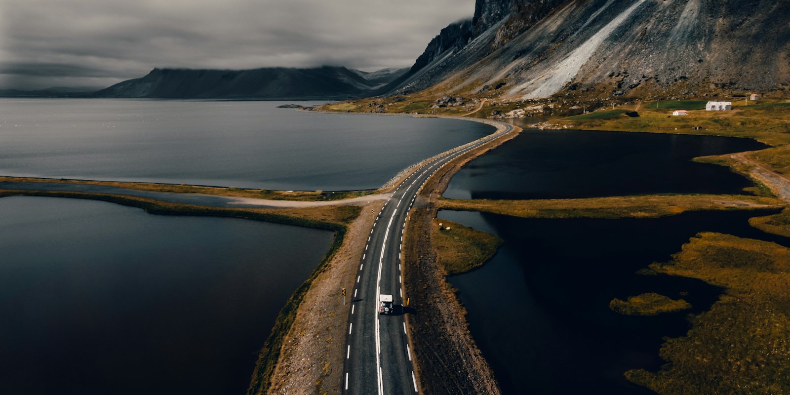 A road crossing water on a causeway below mountains in Iceland