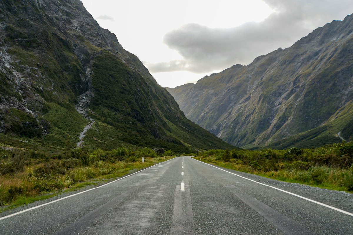 An empty two-lane road running between steep mountain slopes on New Zealand's South Island