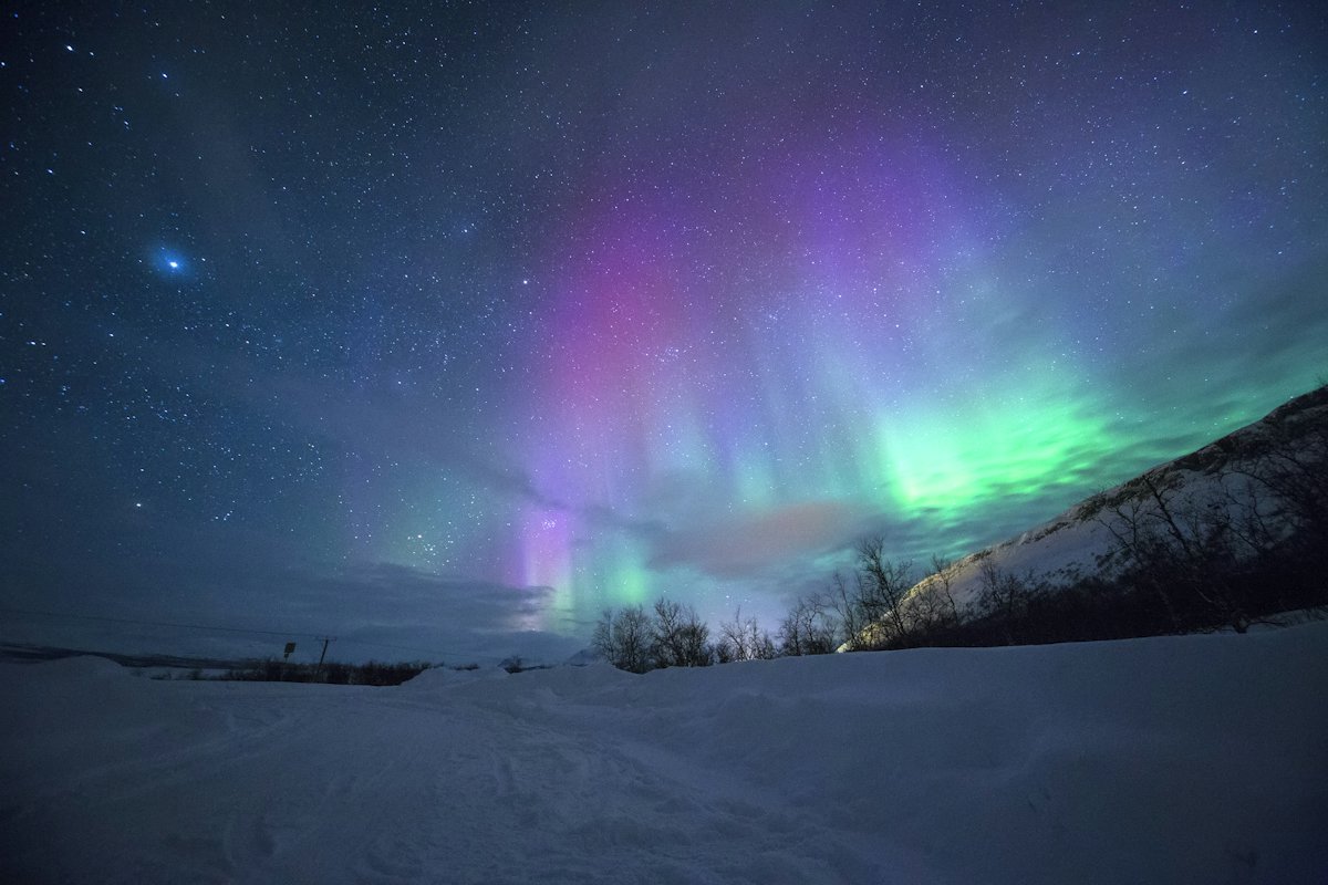 Green and purple aurora over snowy hills near Tromsø