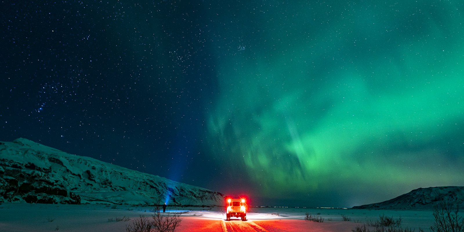 Green aurora over a snowy road with a vehicle's lights below
