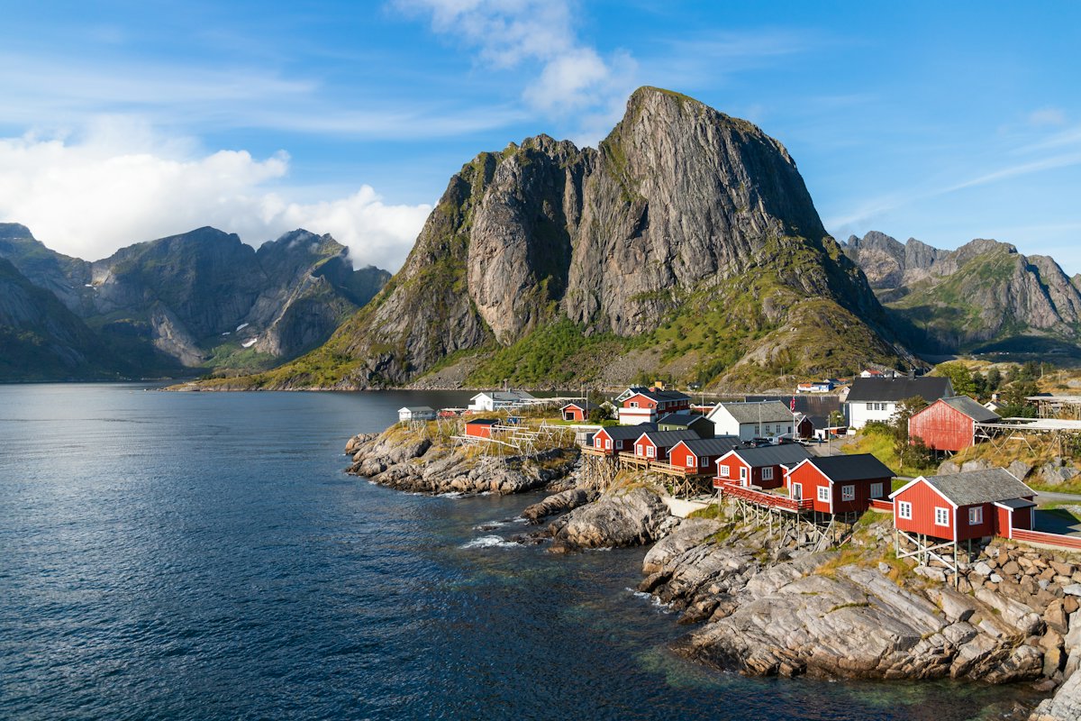 Red fishing cabins at the water's edge below a steep peak in Hamnøy, Lofoten
