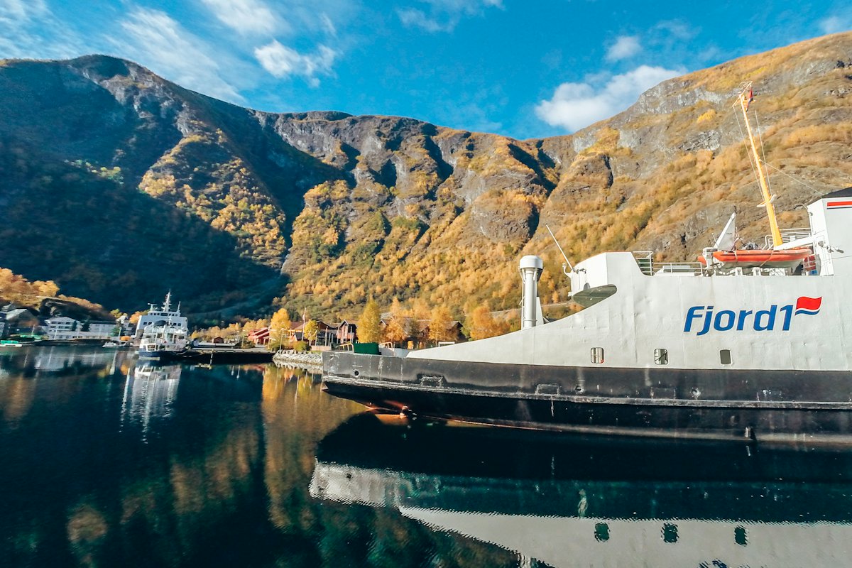 A car ferry moored at a fjord-side quay below autumn mountains in Flåm