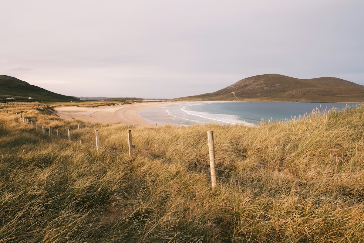 A wide sandy beach with dune grass and hills across the bay in Scotland