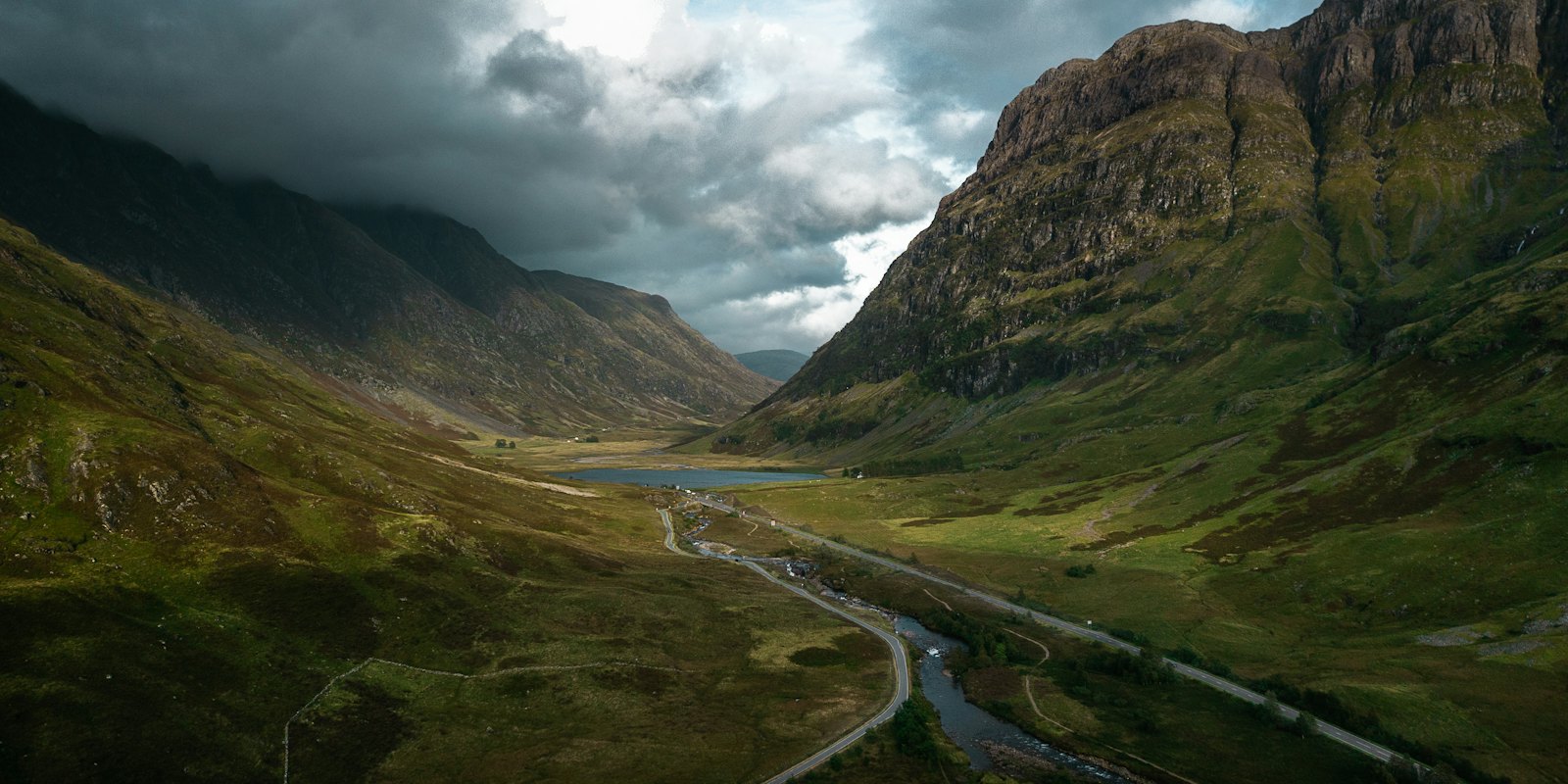 A road winding through a green Highland glen under cloud, Scotland