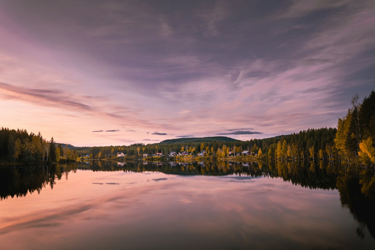 A calm lake reflecting forest and a pink sky at dusk in Sweden