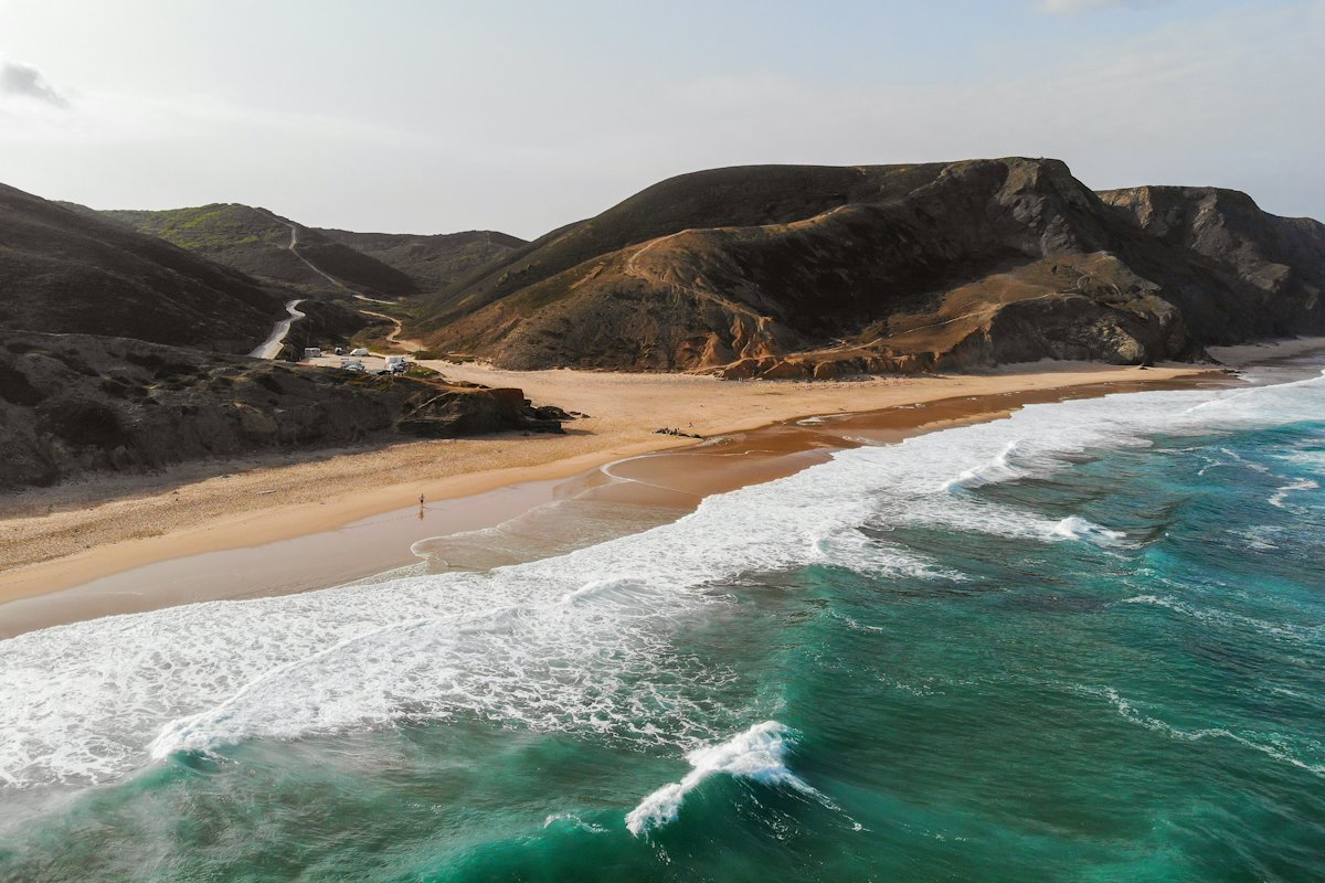 Waves breaking on a wide beach below hills on the Portuguese coast